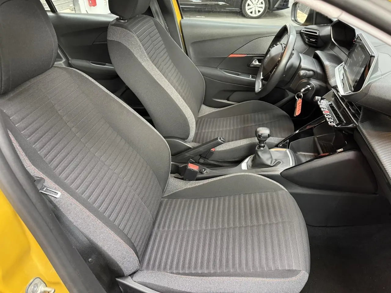 Intérieur de la Peugeot 208 essence jaune clair, vue côté gauche montrant sièges tissu gris et tableau de bord moderne.