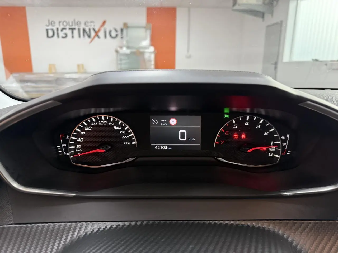 Vue rapprochée du tableau de bord numérique de la Peugeot 208 1.2i PureTech 100, affichant 42103 km et vitesse à 0 km/h.