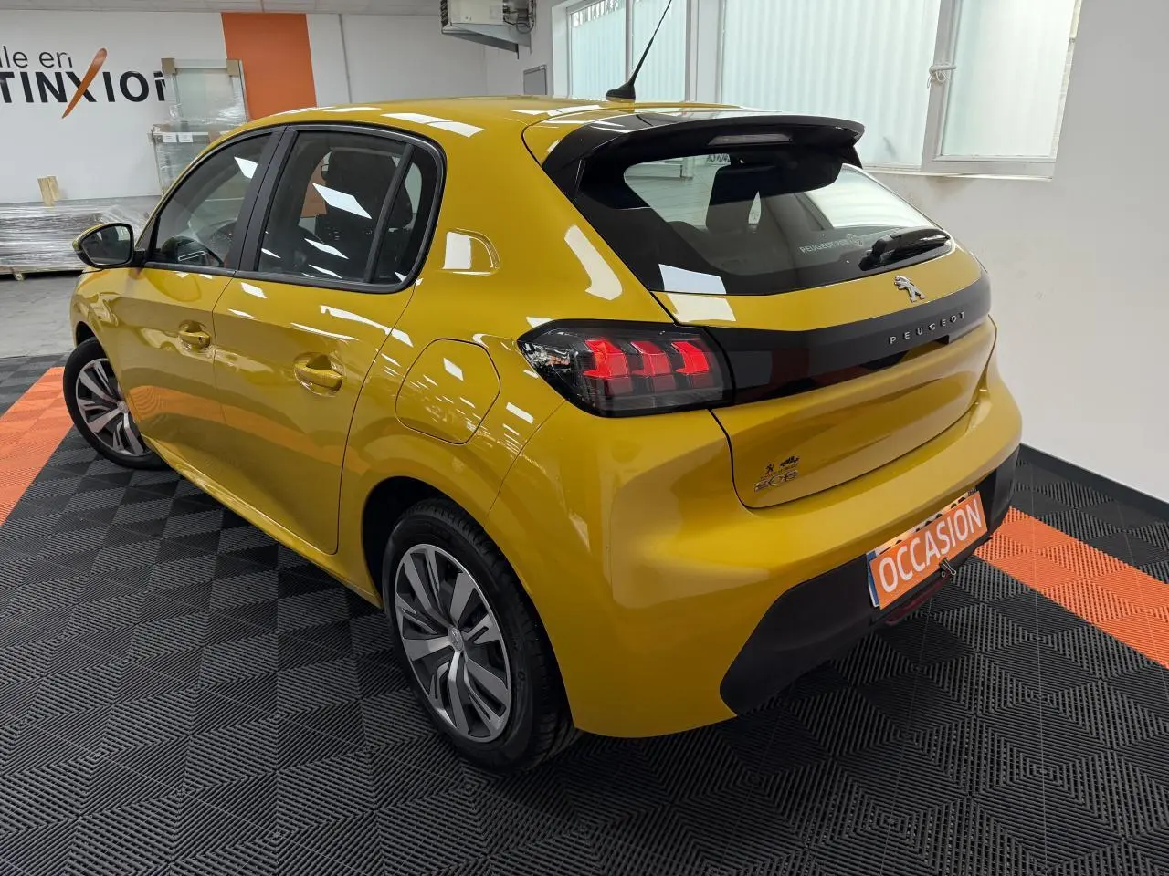 Vue 3/4 arrière droite d'une Peugeot 208 jaune clair avec feux arrière à griffes et jantes alliage modernes.