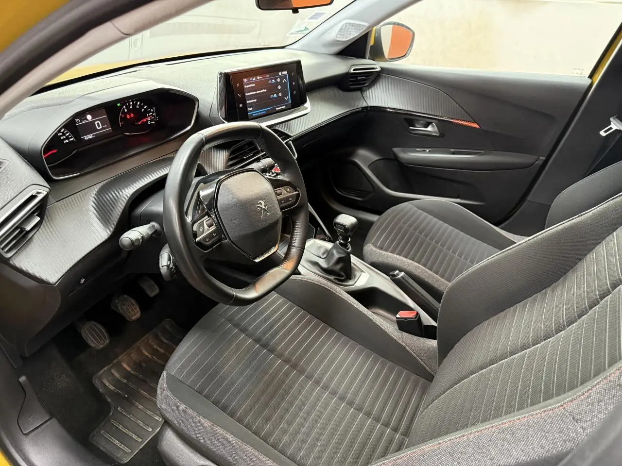 Intérieur avant droit de la Peugeot 208 jaune clair 2020, volant compact, écran tactile et boîte manuelle visibles.