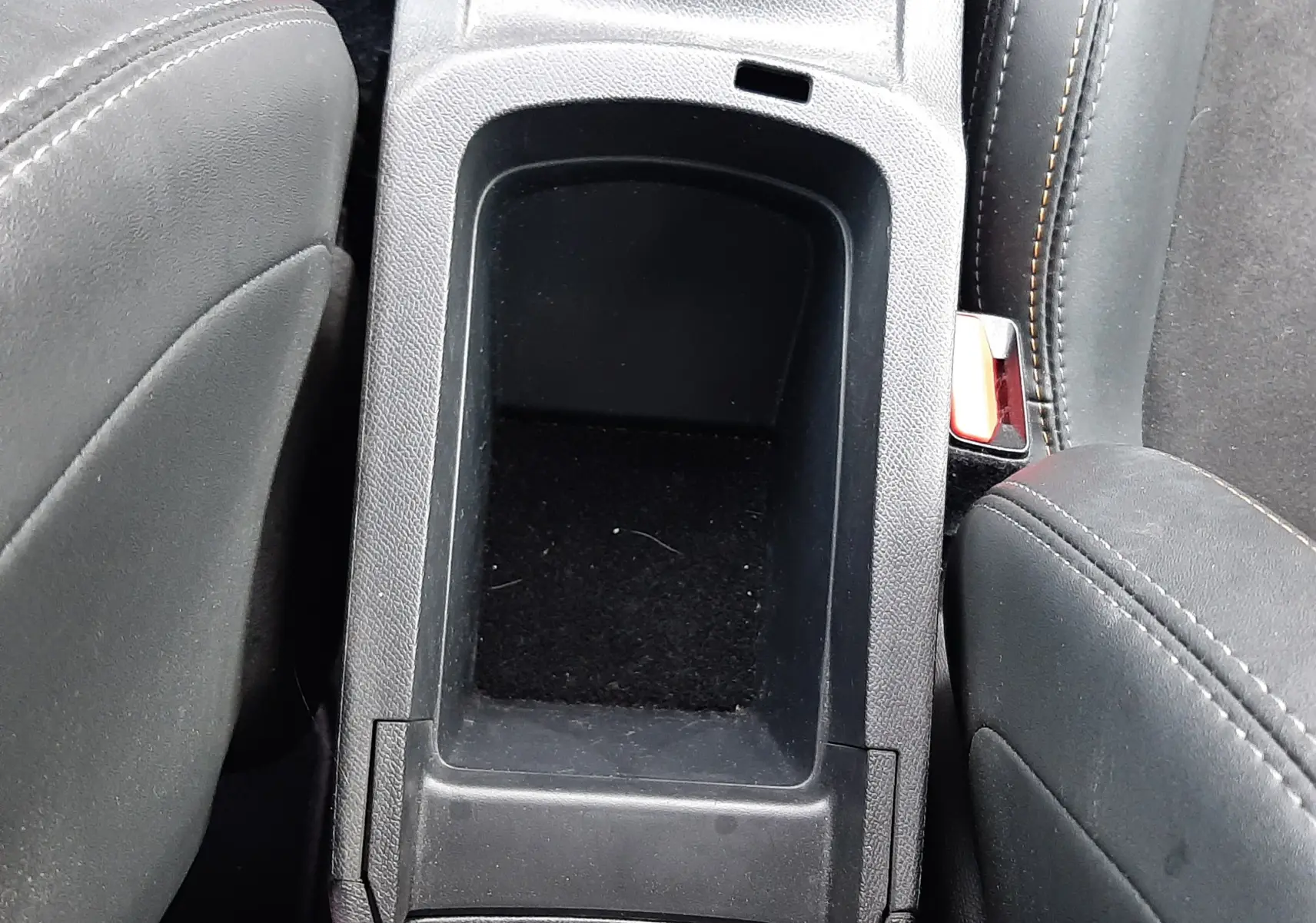 Vue plongeante sur le rangement central noir entre les sièges avant en tissu gris foncé du Peugeot 308 SW 2021.