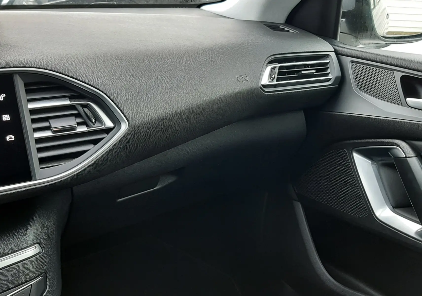 Vue intérieure côté passager de la Peugeot 308 SW 2021 gris Artense, avec tableau de bord et aérateurs noirs.