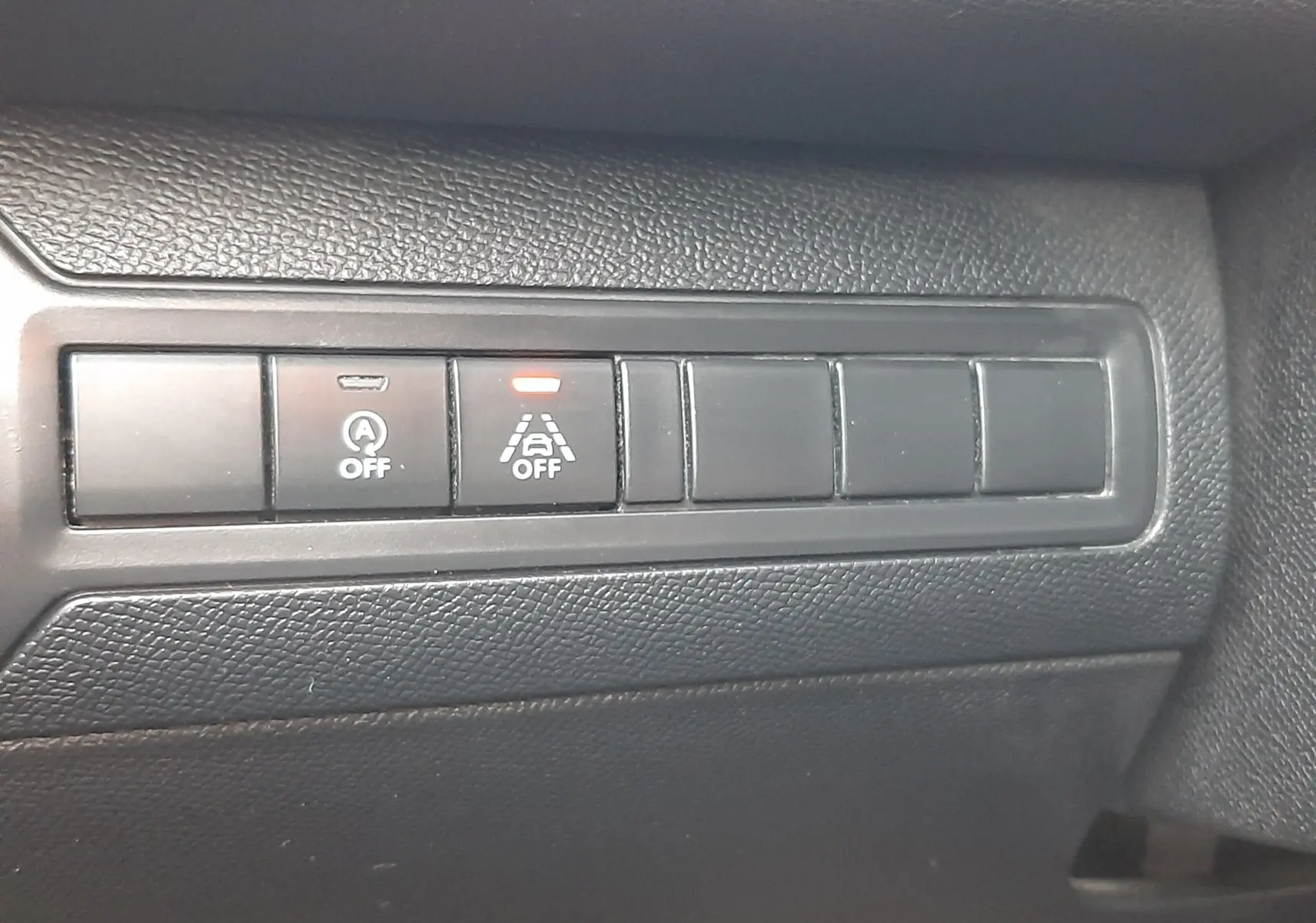 Gros plan sur les boutons de commande noirs du tableau de bord intérieur de la Peugeot 308 SW gris Artense, avec témoin lumineux orange allumé.