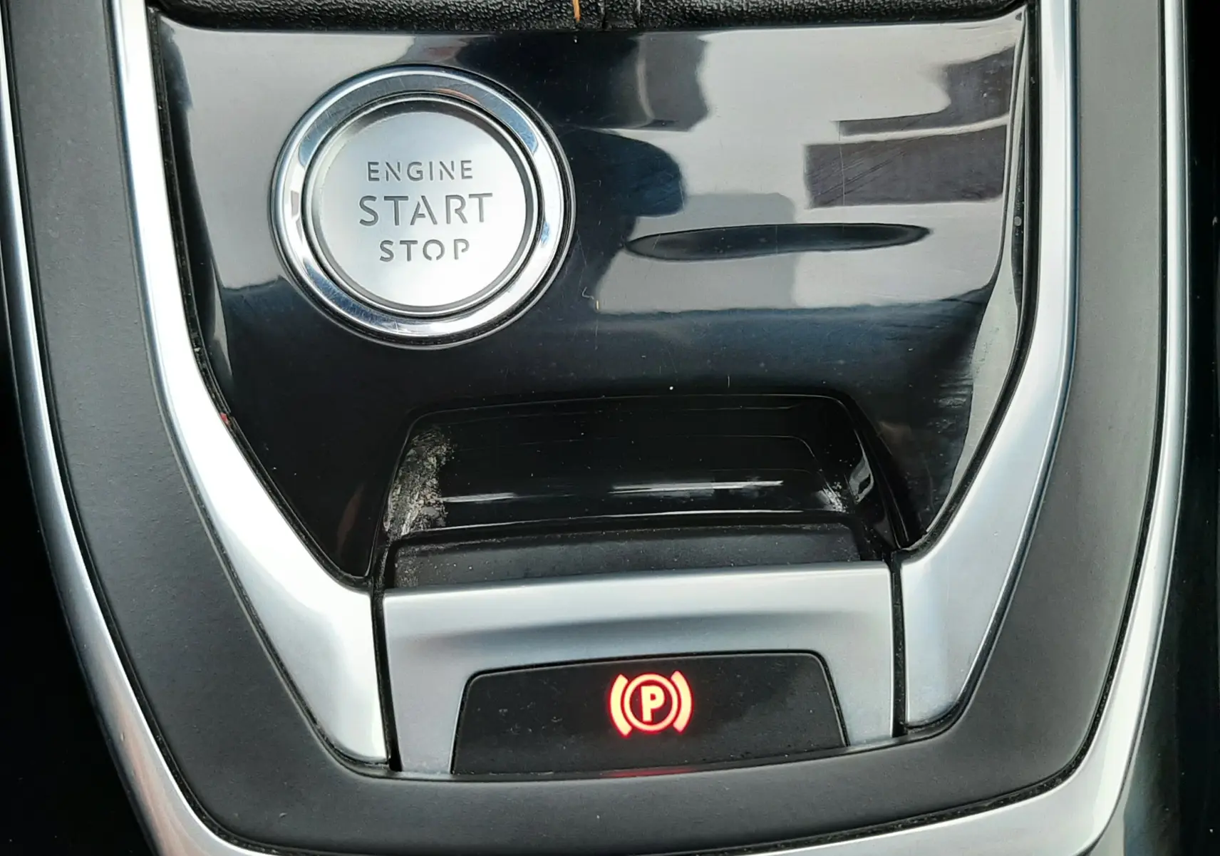 Gros plan sur le bouton start/stop et le frein à main électronique rouge dans la console centrale noire brillante d'une Peugeot 308 SW.
