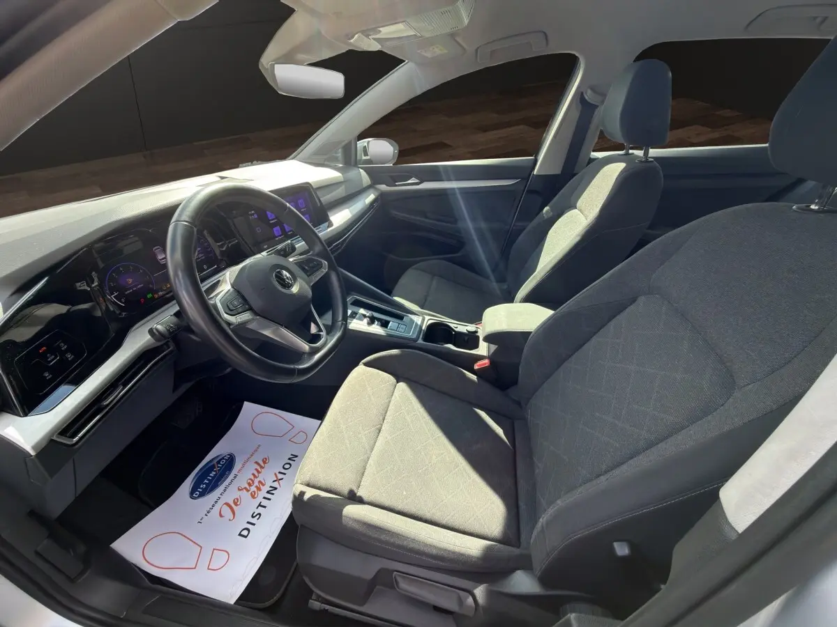 Intérieur avant droit de la Volkswagen Golf gris clair 2022, avec tableau de bord numérique et volant cuir multifonctions.