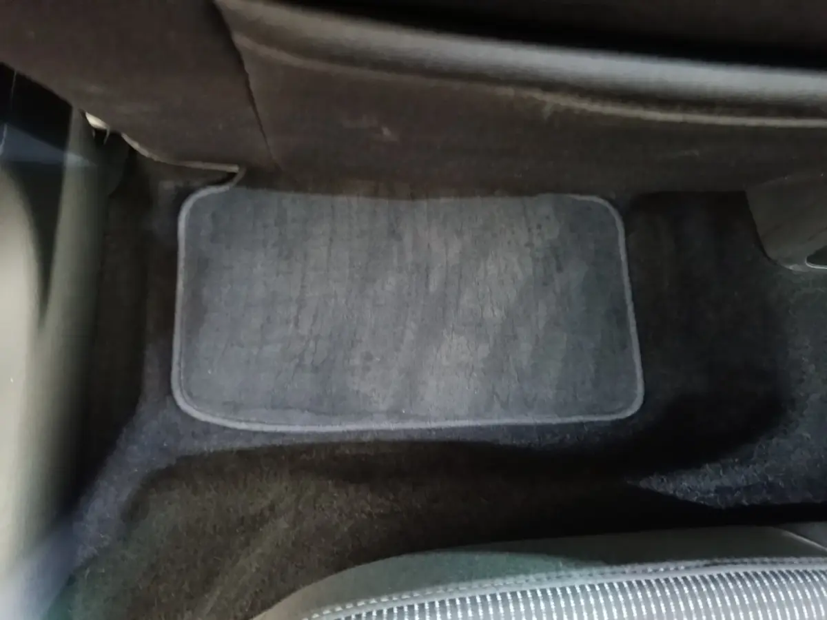 Vue intérieure du plancher arrière avec tapis de sol gris et siège tissu noir partiel d'une Skoda Octavia 2024.