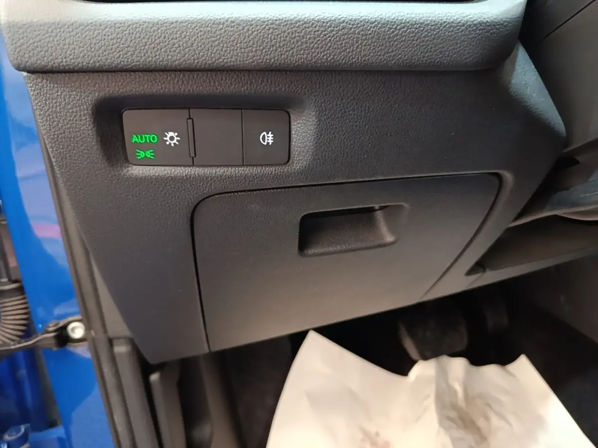 Détail intérieur côté gauche avec commandes d’éclairage activées en vert, partie de la carrosserie bleue visible.