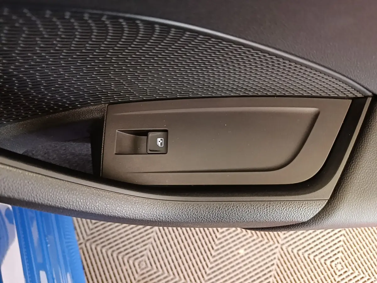 Détail de la commande de lève-vitre sur la porte côté conducteur d’une Skoda Octavia 2024 bleu visible en bas.