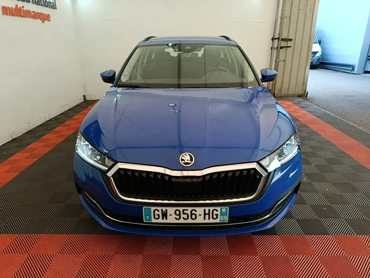 Vue avant d'une Skoda Octavia 2024 bleue avec calandre noire et phares LED, stationnée en intérieur sur sol à damier rouge et noir.