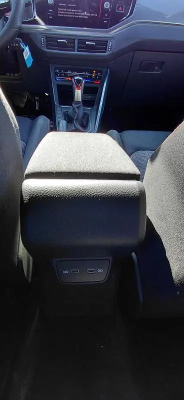 Vue intérieure centrée sur l'accoudoir central et la console de la Volkswagen Polo GTI noire 2024 avec commandes et ports USB visibles.