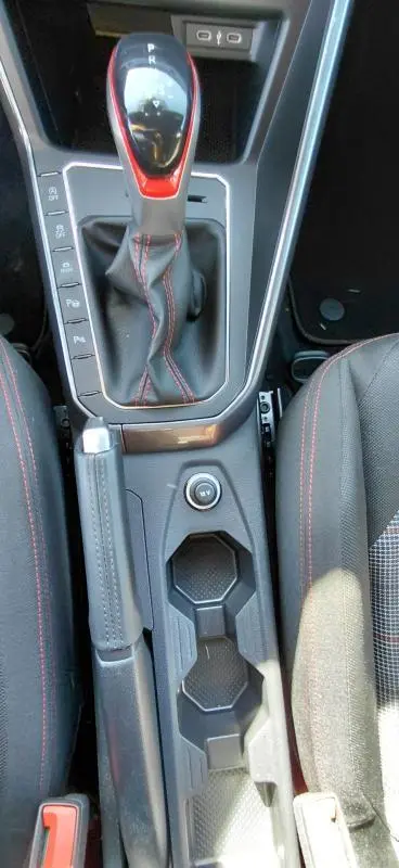 Vue plongeante sur la console centrale de la Volkswagen Polo GTI 2024 noire, avec levier de vitesse DSG7 et coutures rouges sport.