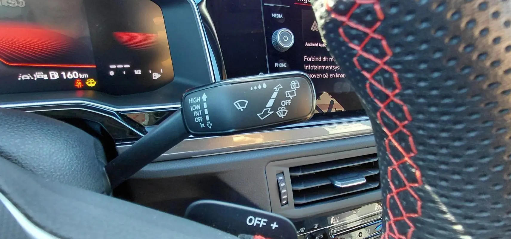 Gros plan sur la commande des essuie-glaces et volant sport avec surpiqûres rouges dans l’habitacle d’une Volkswagen Polo GTI 2024.