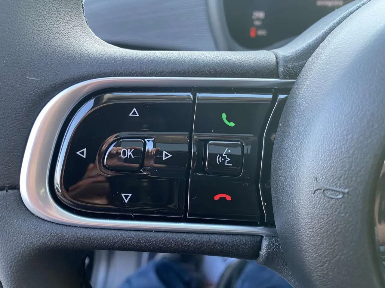 Gros plan sur les commandes du volant côté gauche de la Fiat 500 électrique noire, avec boutons de téléphone et navigation.