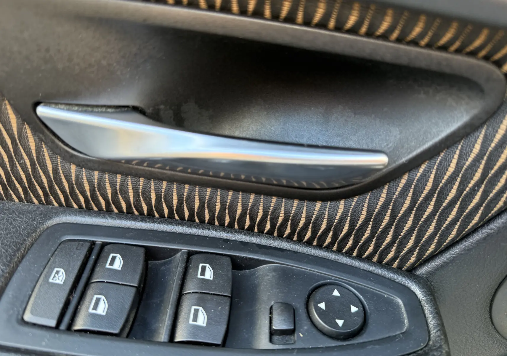 Gros plan sur la poignée intérieure et les commandes de vitres électriques côté conducteur d'une BMW Série 3 320D gris avec tissu rayé.