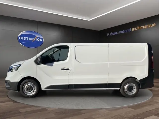 Vue latérale droite d'un Renault Trafic Fourgon blanc 2023, version L2H1 Grand Confort avec kit bois, sur fond intérieur showroom.