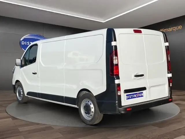 Vue 3/4 arrière droite d’un Renault Trafic Fourgon blanc 2023 avec kit bois, dans un showroom intérieur.