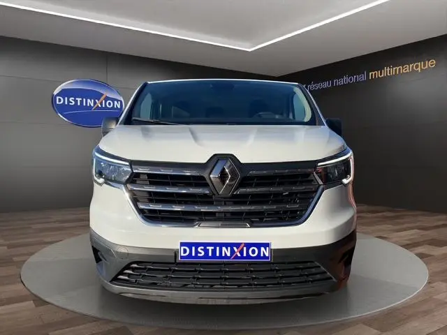 Vue frontale d'un Renault Trafic Fourgon blanc 2023 avec calandre noire et logo Renault centré, en showroom.
