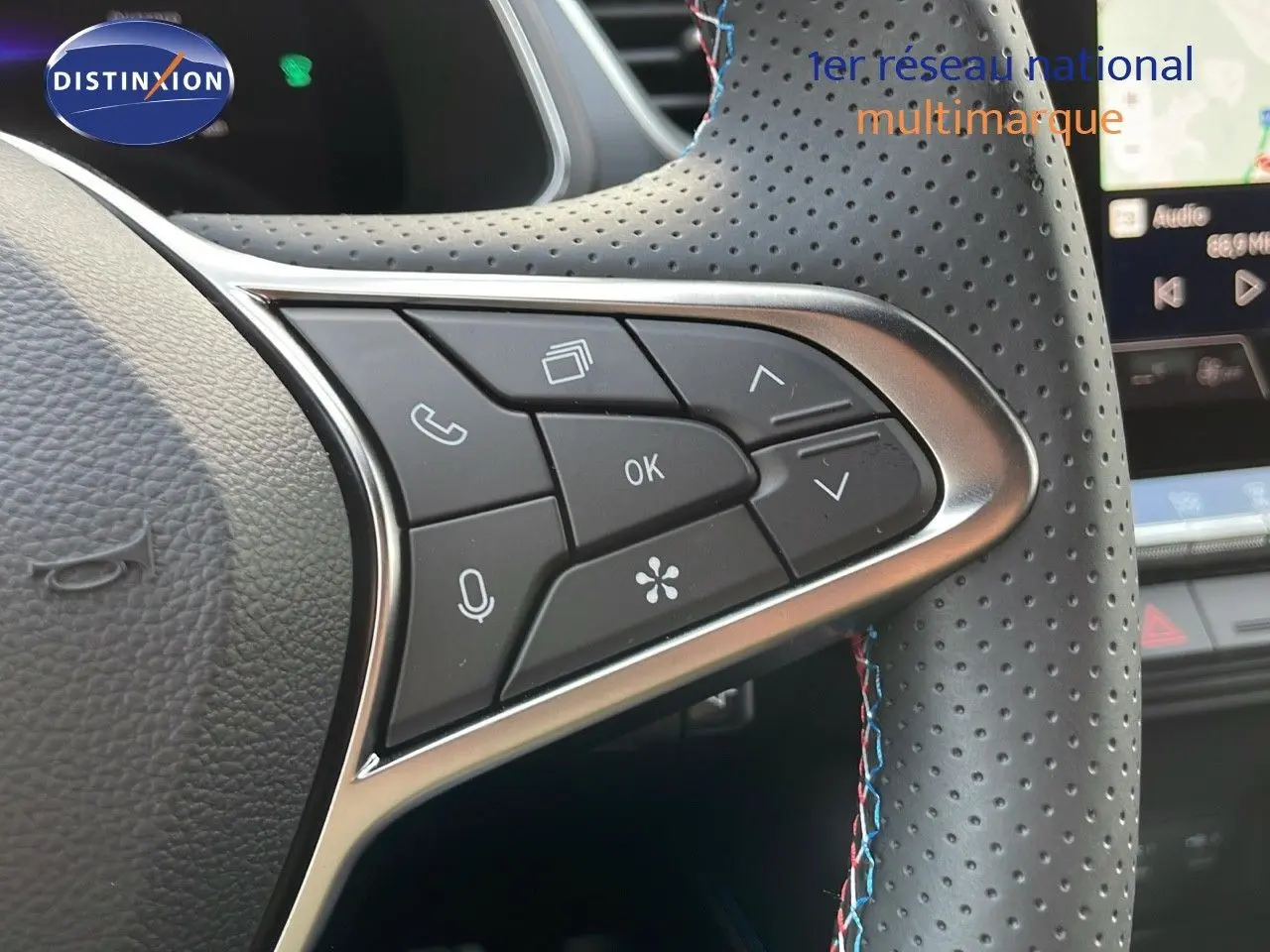 Gros plan sur les commandes du volant en cuir noir perforé avec surpiqûres bleues du Renault Captur E-Tech hybride 2025.