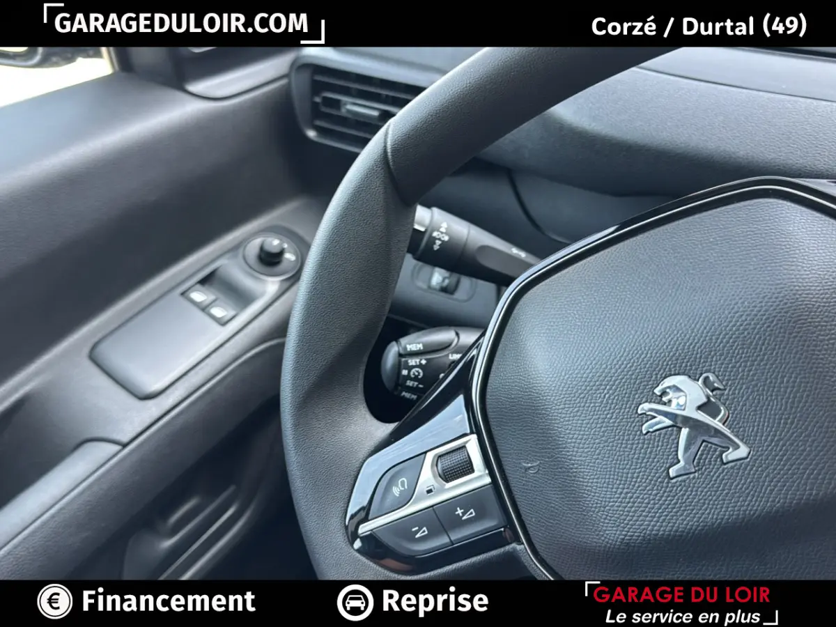 Vue rapprochée du volant Peugeot avec logo lion et commandes intégrées, côté gauche de l’habitacle noir.