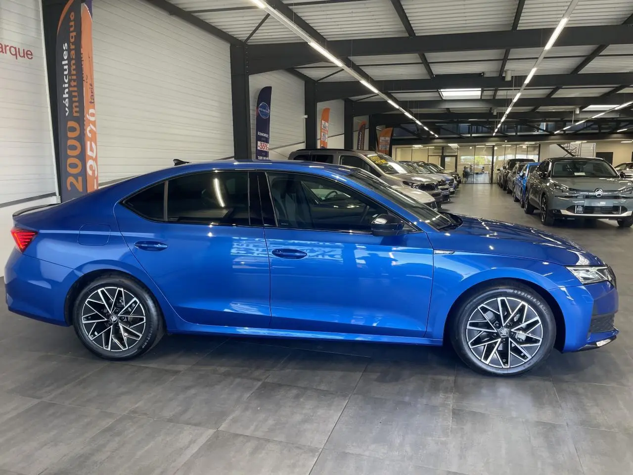 Vue latérale droite d'une Skoda Octavia 2025 bleu foncé avec jantes alliage noires et vitres teintées dans un showroom.
