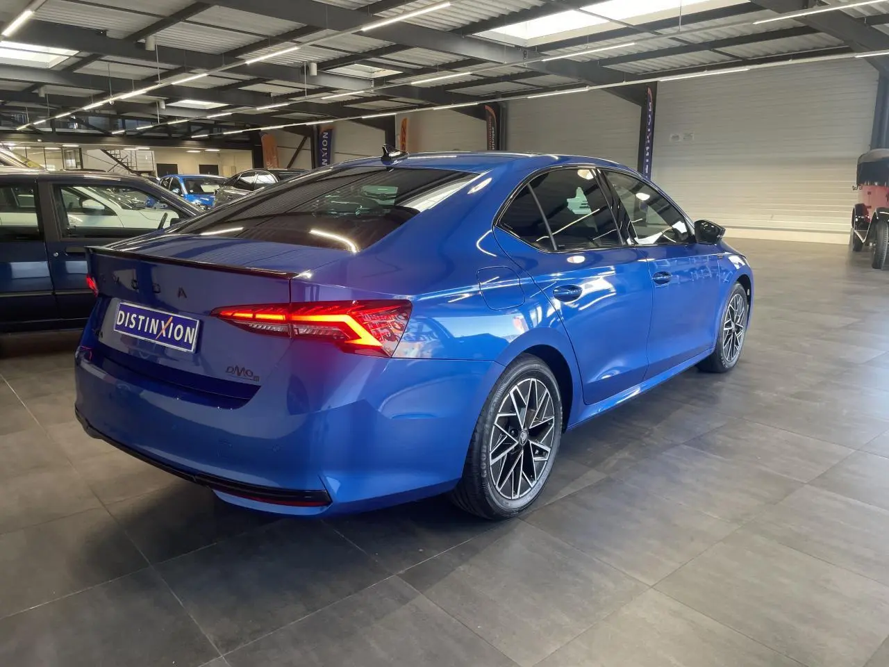 Vue 3/4 arrière droite d'une Skoda Octavia Sportline bleu foncé avec jantes alliage noires et feux arrière LED allumés.