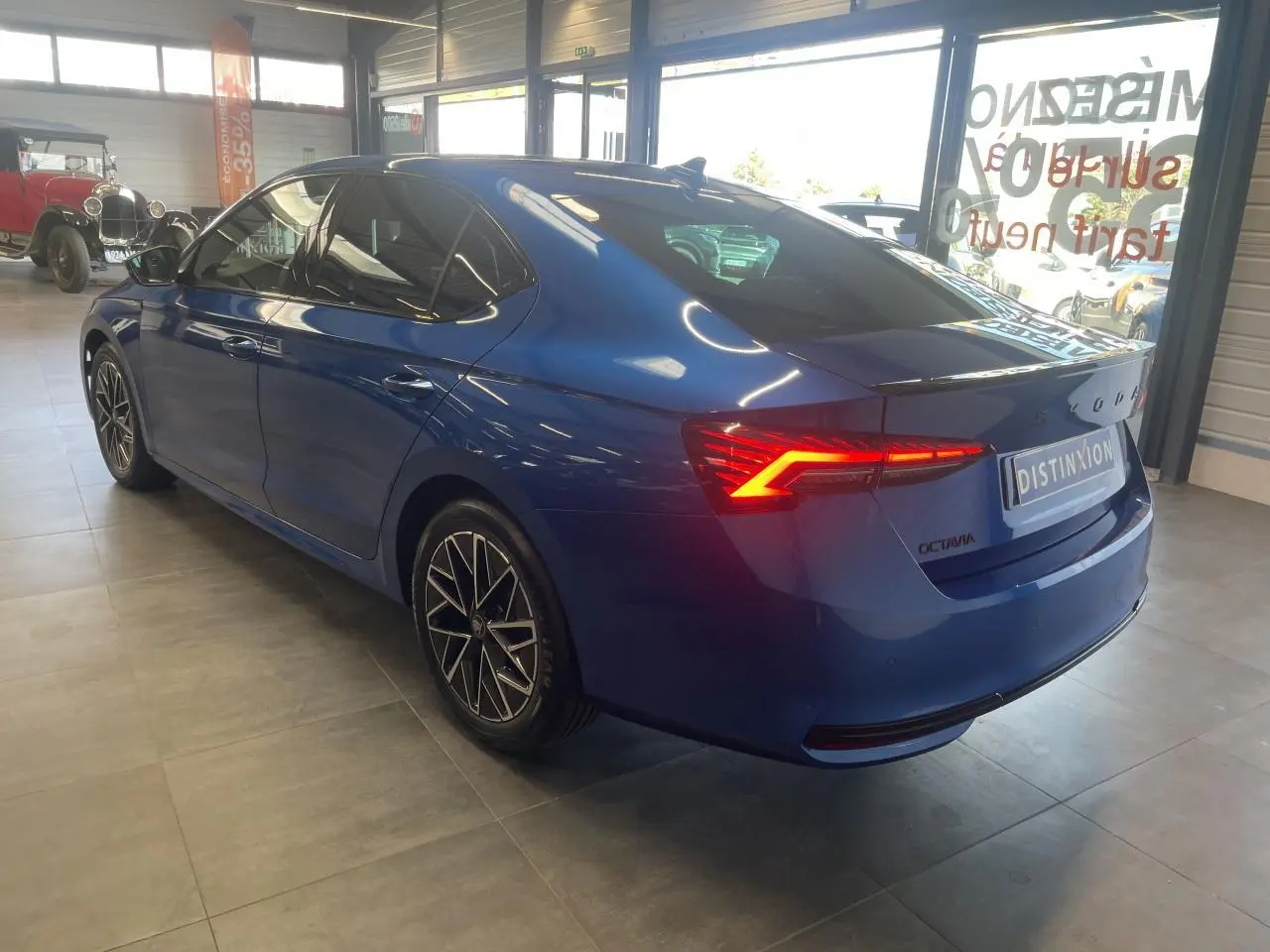 Vue 3/4 arrière droite d'une Skoda Octavia 2025 bleu foncé avec feux arrière LED allumés en intérieur showroom.