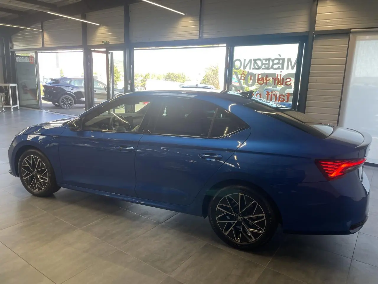 Skoda Octavia 2025 bleu foncé vue de profil côté gauche en intérieur avec feux arrière allumés et jantes alliage noires.