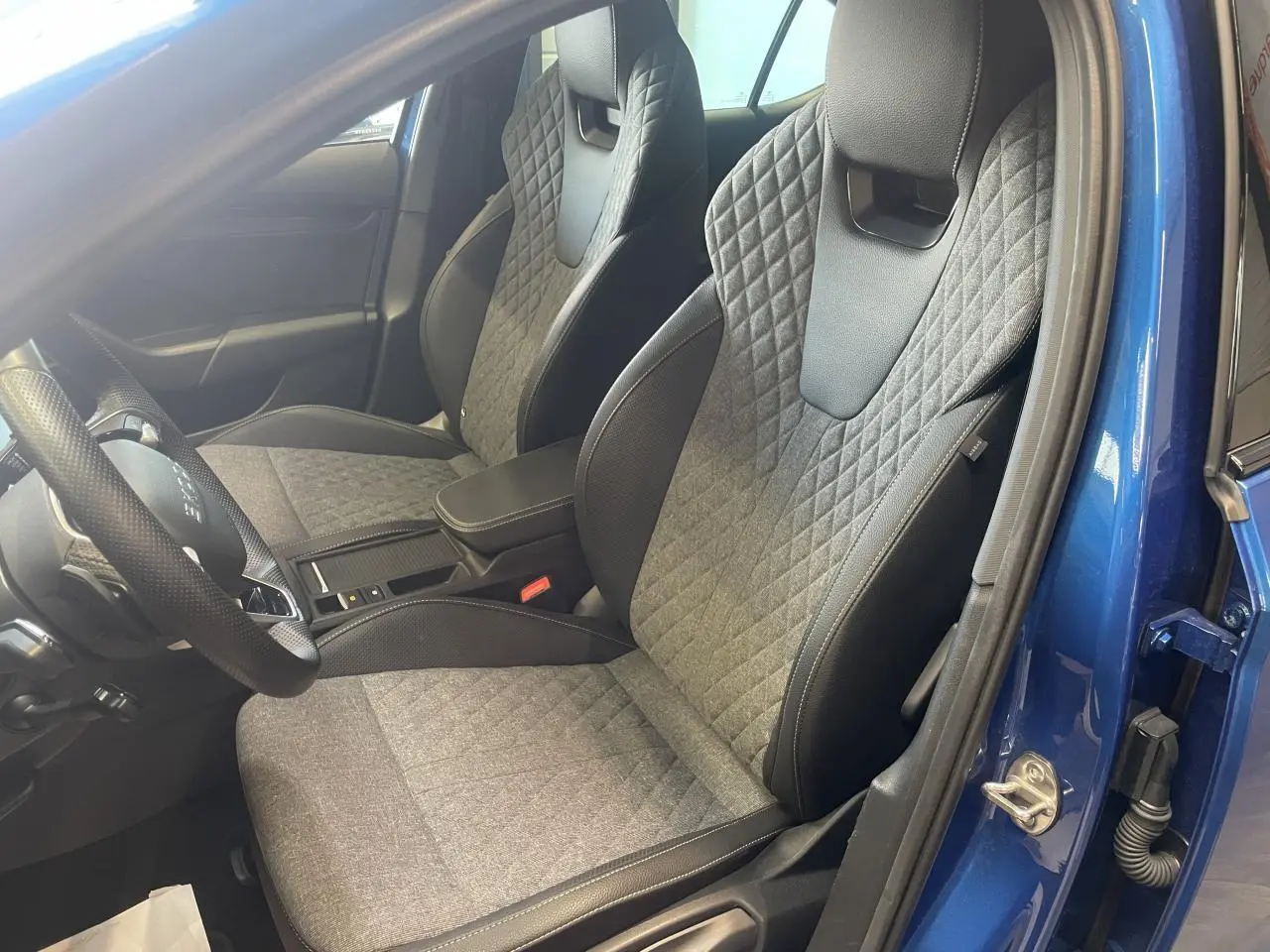 Intérieur avant de la Skoda Octavia bleu foncé 2025, sièges sport gris avec surpiqûres losanges et volant cuir.