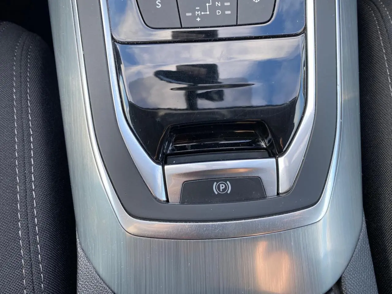 Gros plan sur la console centrale de la Peugeot 308 gris aluminium, mettant en valeur le frein de parking électrique et la finition métallique.
