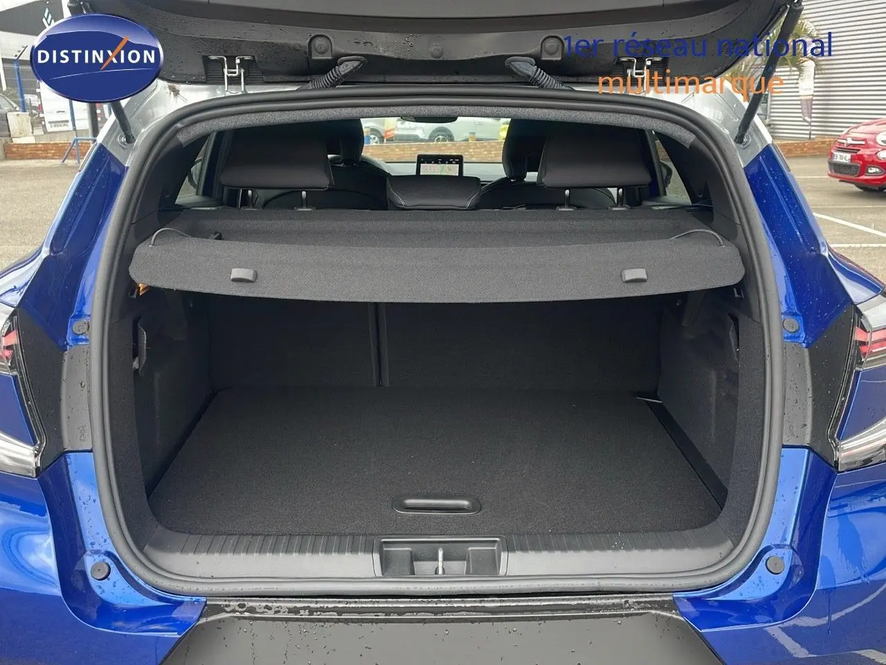 Coffre ouvert d'un Renault Captur E-Tech hybride bleu Iron Metal avec toit gris, vue arrière montrant l'espace de chargement.