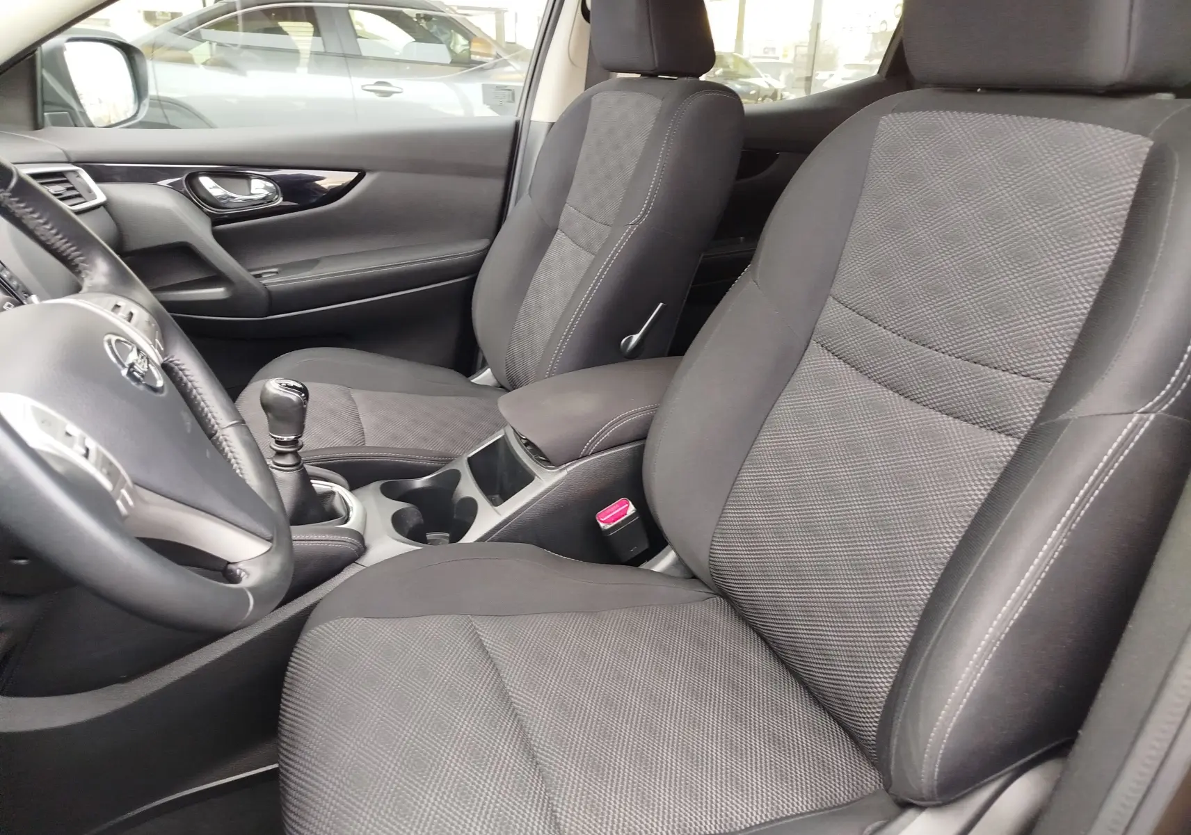 Vue intérieure côté conducteur du Nissan Qashqai 2017, tableau de bord noir avec écran tactile et boîte manuelle.