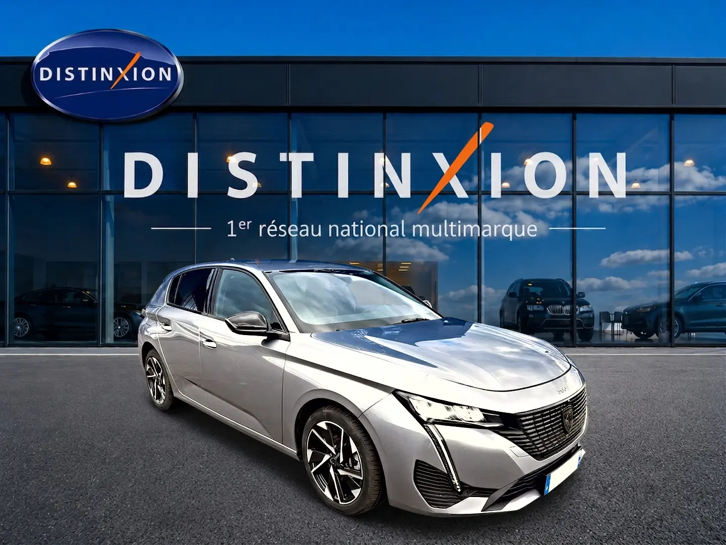 Peugeot 308 gris artense vue 3/4 avant droit, avec jantes alu et feux LED distinctifs, devant showroom Distinxion.