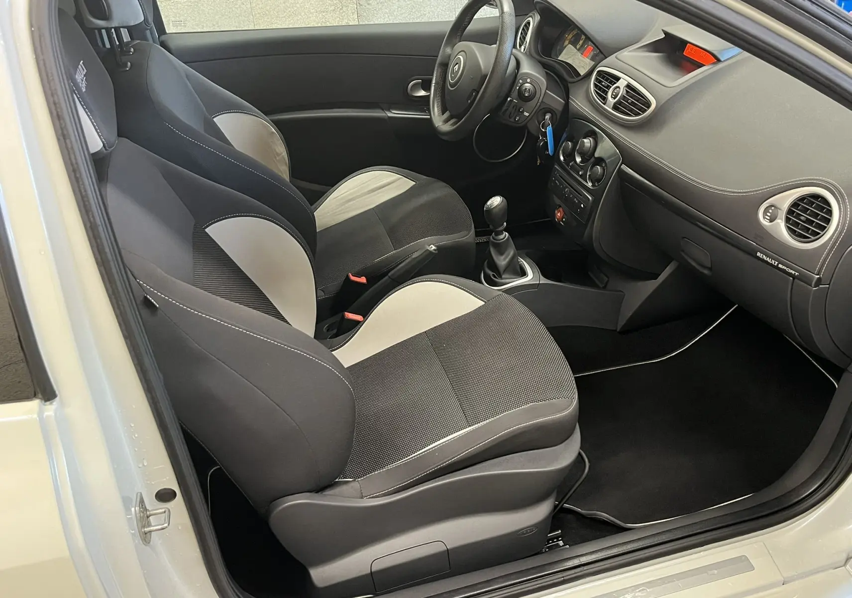 Vue intérieure côté conducteur de la Renault Clio III RS 20th Anniversary avec sièges sport bicolores noir et gris.