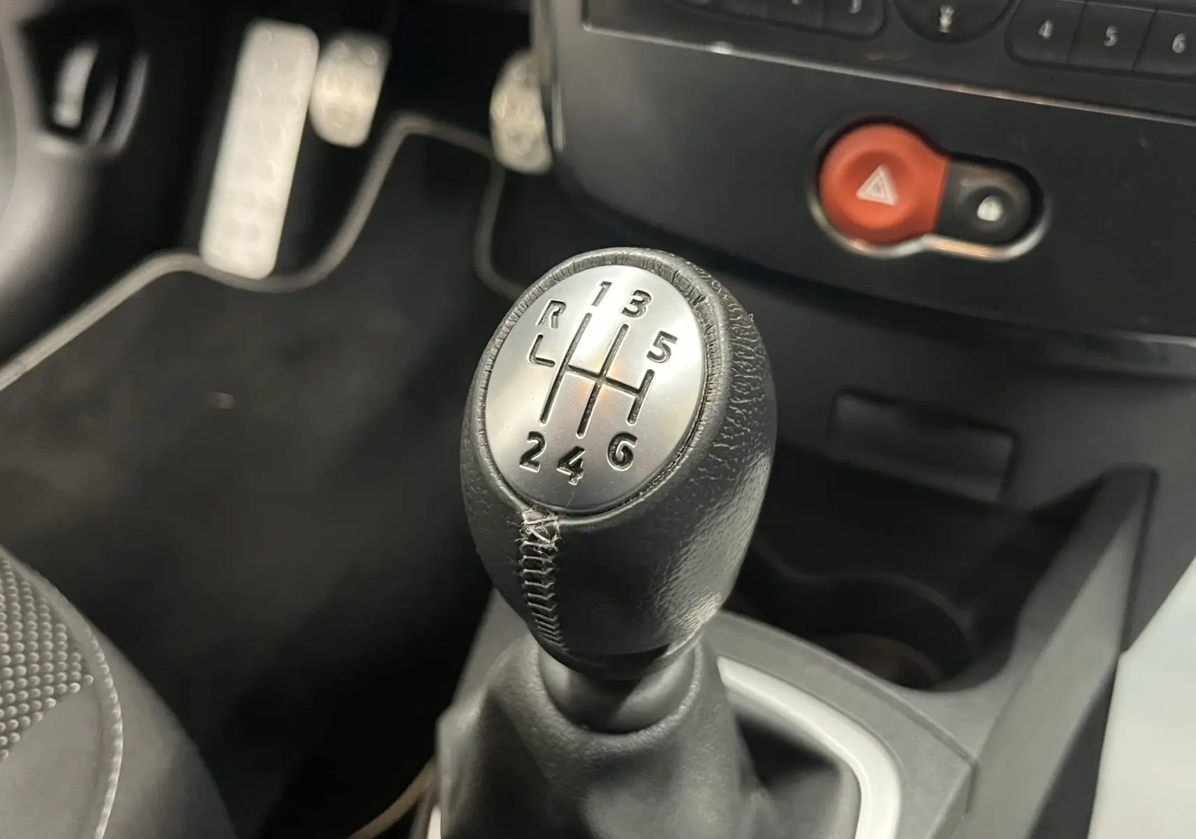 Gros plan sur le levier de vitesses manuel noir avec marquages argentés dans l'habitacle sombre d'une Renault Clio III RS.