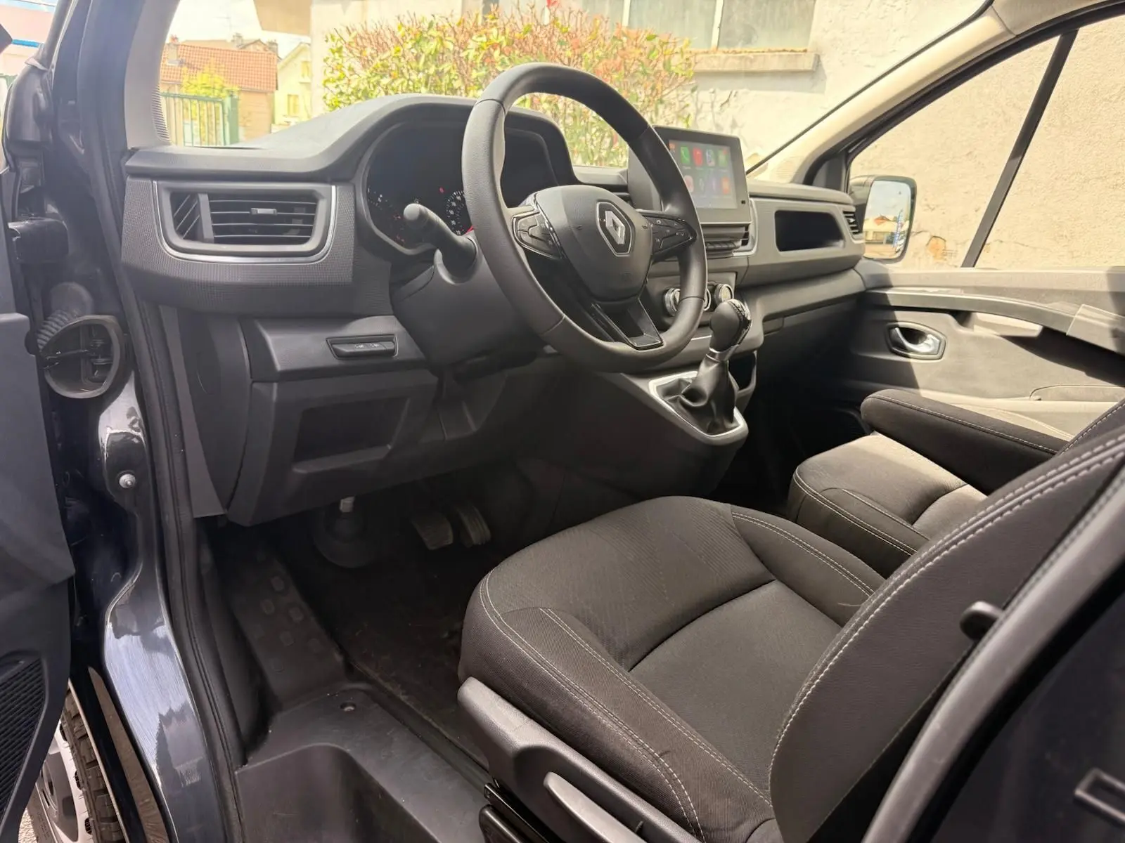 Vue intérieure côté conducteur du Renault Trafic gris comète, montrant le volant multifonction et la console centrale avec écran tactile.