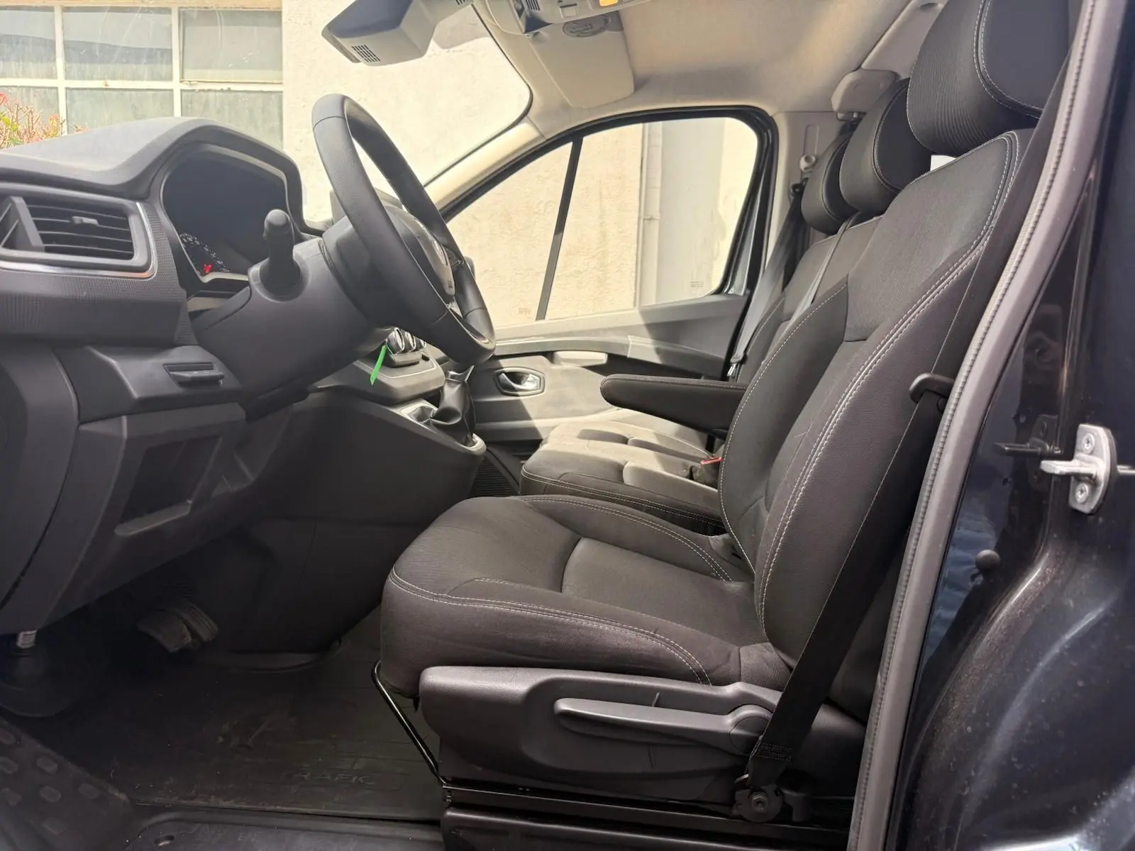 Vue intérieure côté conducteur du Renault Trafic cabine approfondie 2024, sièges tissu gris et tableau de bord sobre.