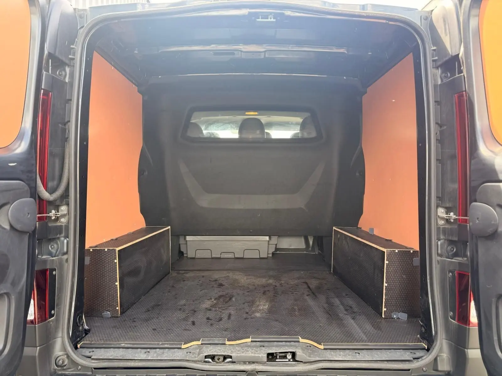Vue arrière du Renault Trafic cabine approfondie gris comète, montrant l'espace de chargement avec habillage bois et plancher antidérapant.