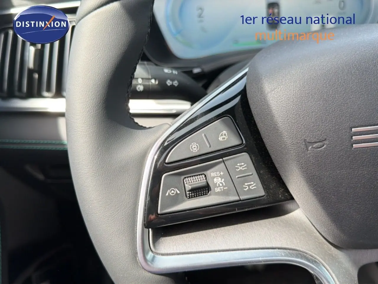 Gros plan sur les commandes à gauche du volant noir du BYD SEAL U hybride rechargeable blanc métal, tableau de bord en arrière-plan.