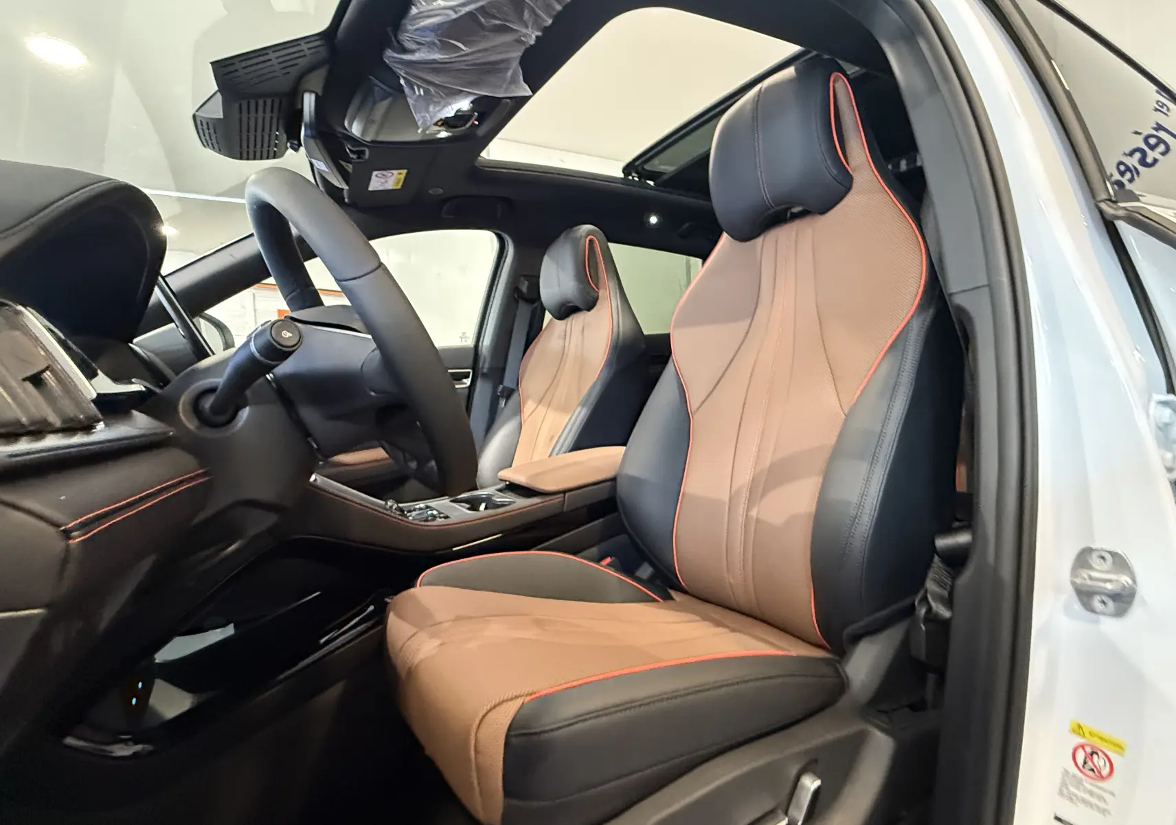 Vue intérieure côté conducteur du BYD SEAL U 2026 blanc métal, sièges cuir bicolore marron et noir avec surpiqûres rouges.