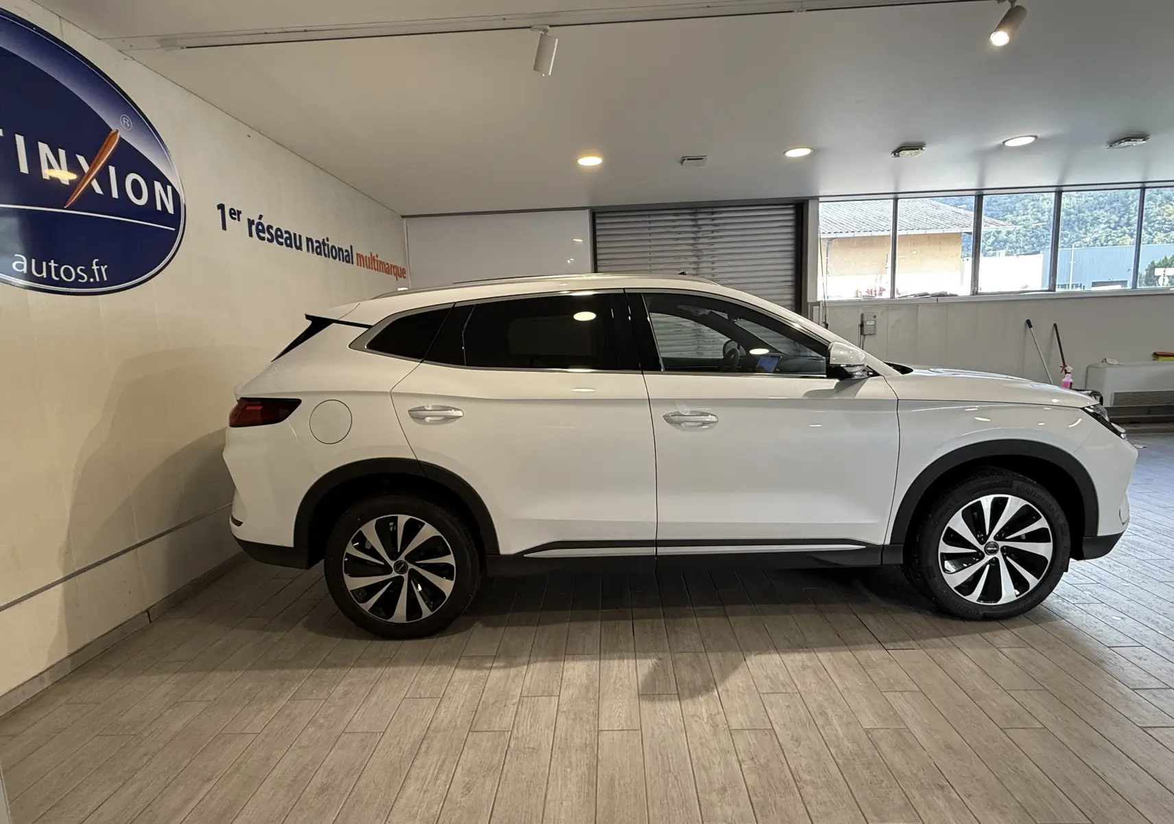 Vue de profil côté gauche d'un SUV BYD SEAL U blanc métal, avec jantes bicolores et vitres teintées, en intérieur showroom.
