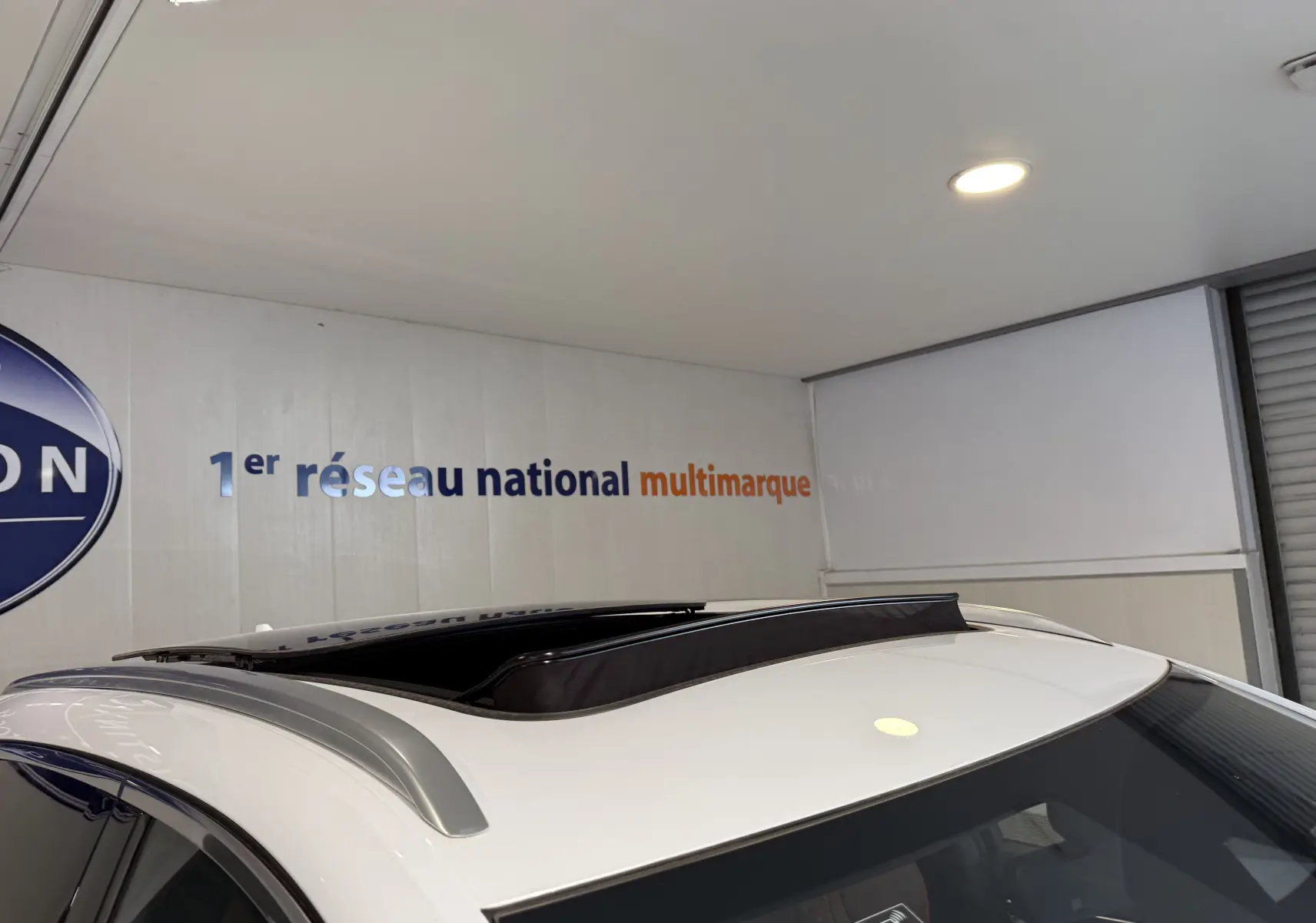 Toit ouvrant panoramique ouvert sur le dessus d’un BYD SEAL U blanc métal, vue partielle en intérieur showroom.