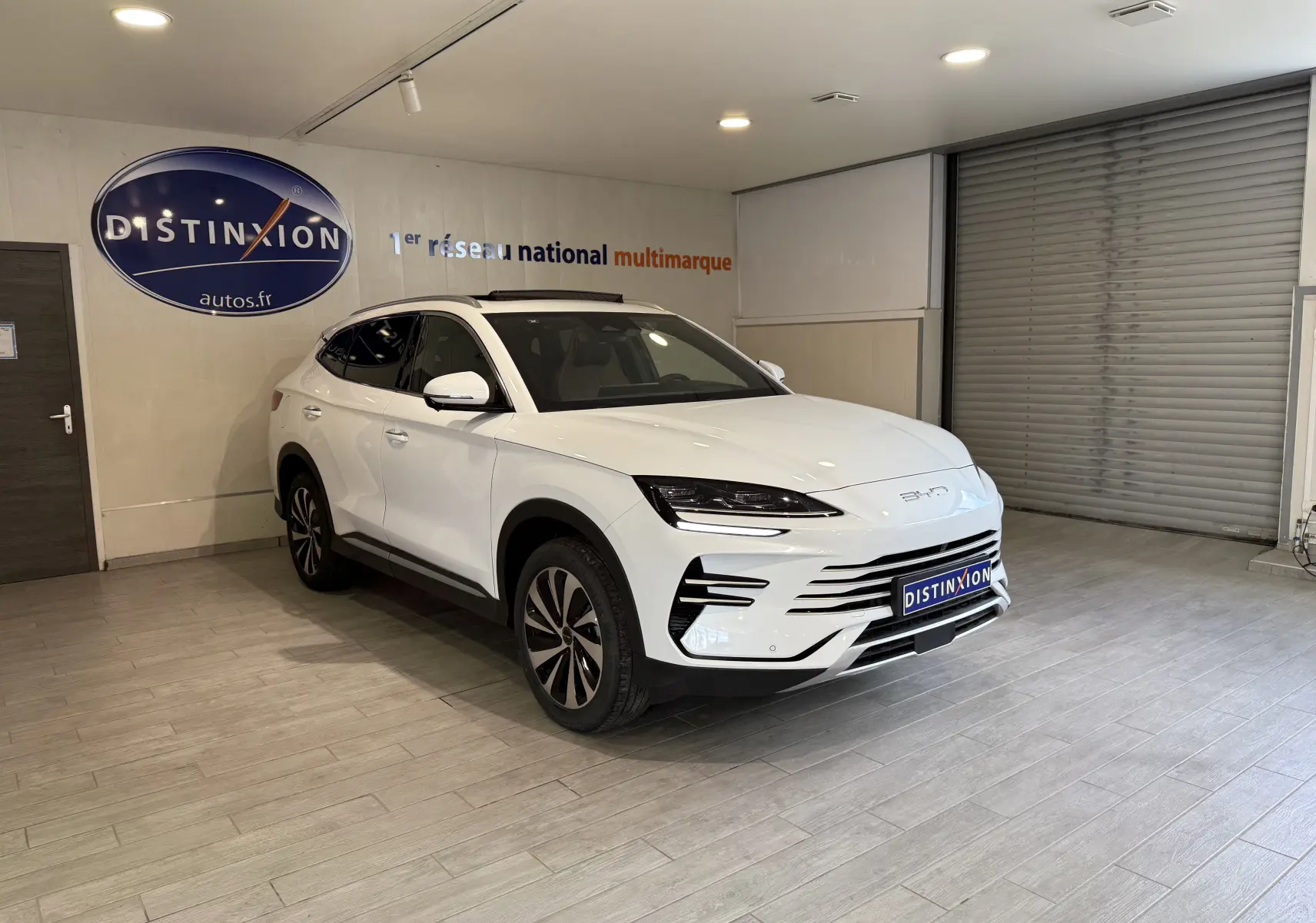 Vue 3/4 avant droite du SUV BYD SEAL U blanc métal, avec calandre moderne et jantes bi-ton, en intérieur showroom.