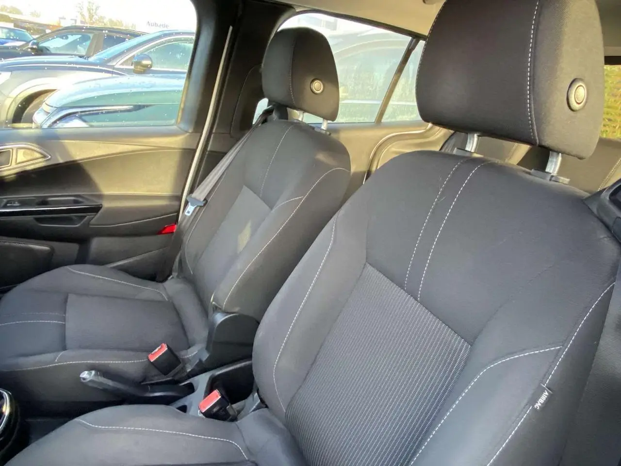 Vue intérieure côté conducteur du Ford B-MAX 2014, sièges noirs avec surpiqûres blanches et ceinture de sécurité visible.