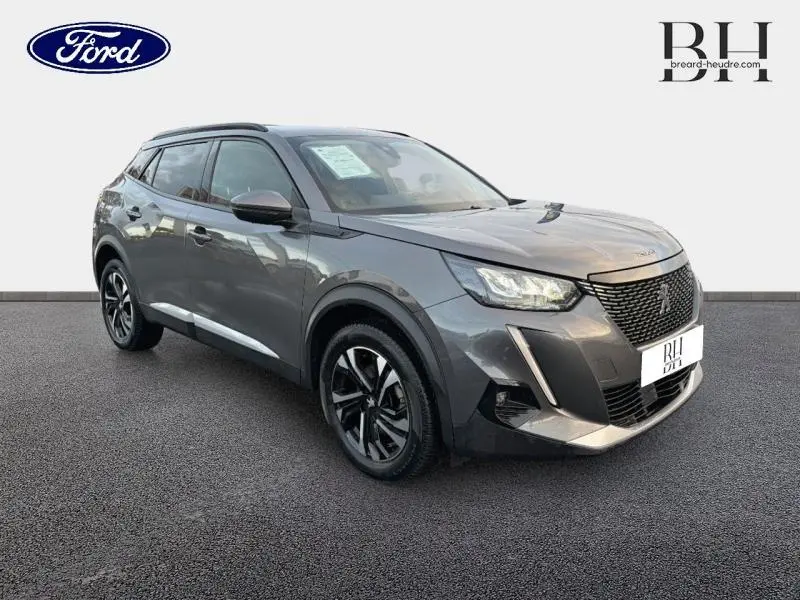 Peugeot 2008 gris Artense vue 3/4 avant droit, avec jantes alliage noires et barres de toit visibles.