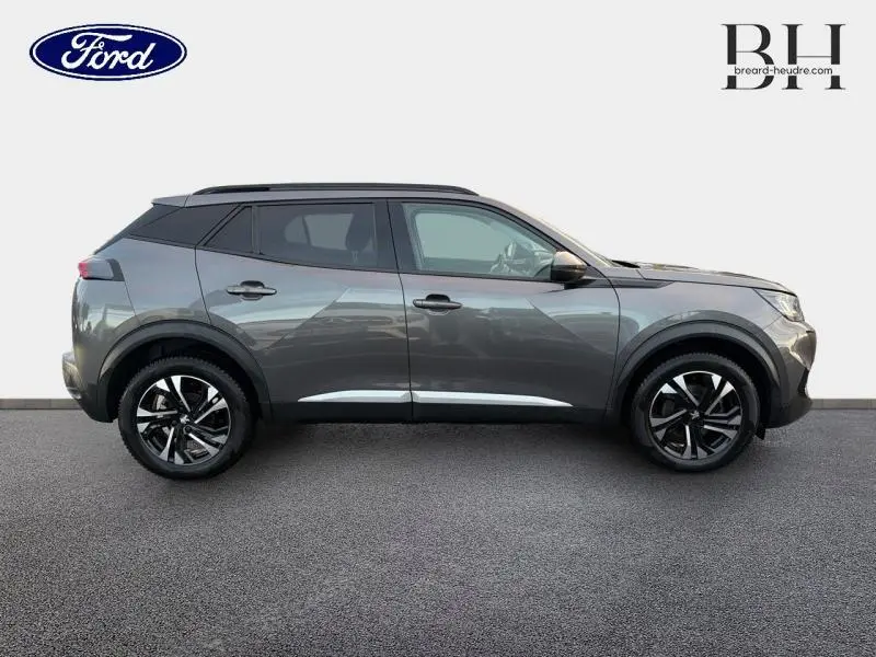 Profil côté droit du Peugeot 2008 gris Artense 2021 avec jantes alliage et barres de toit visibles.