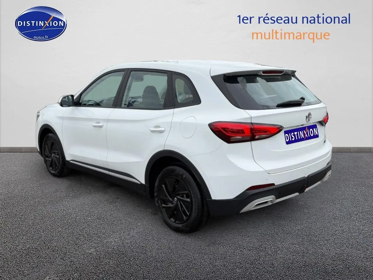 Vue 3/4 arrière droite d'un MG ZS Hybrid blanc avec jantes noires et feux arrière LED sur fond neutre.