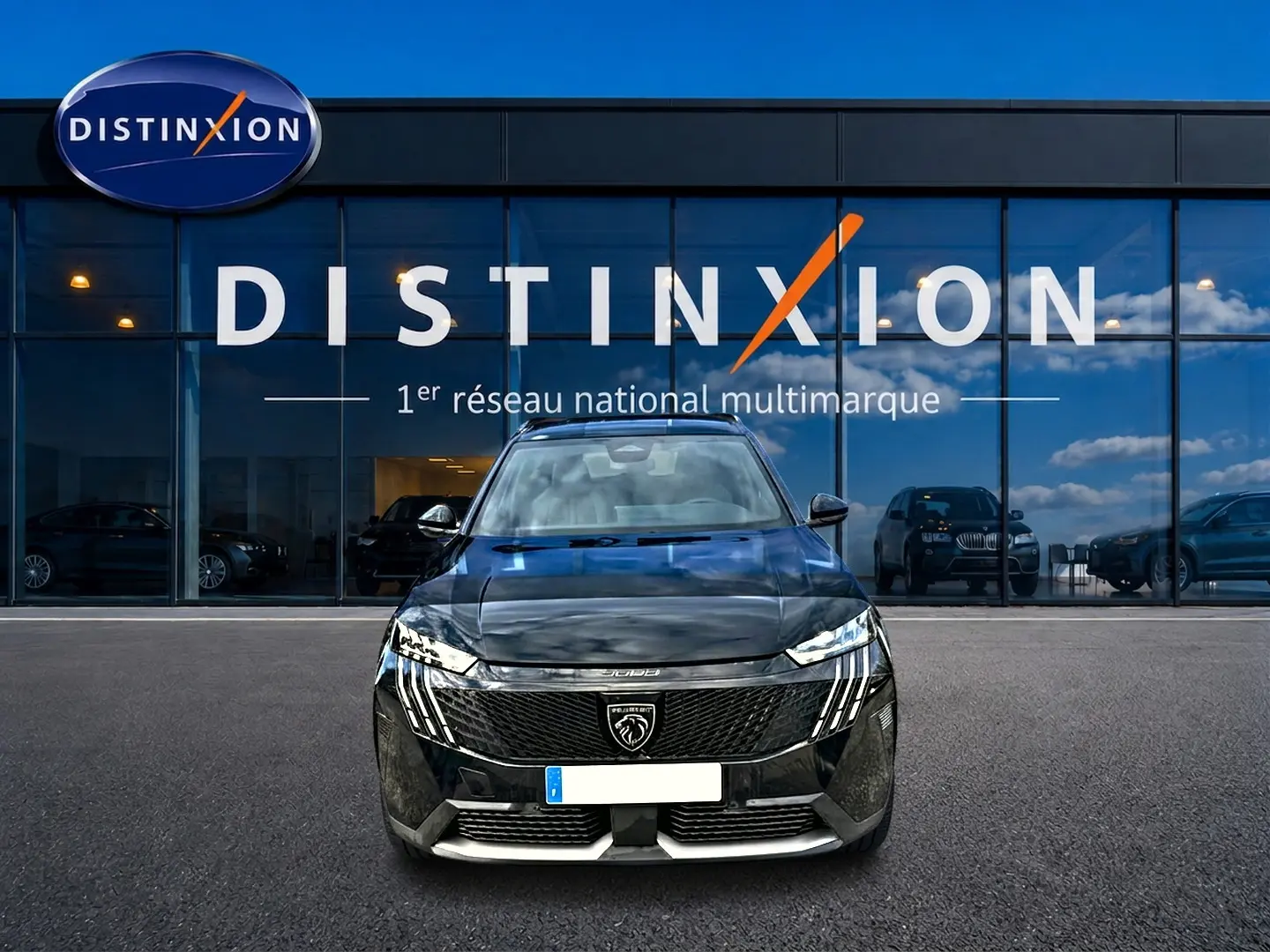 Vue avant d'un Peugeot 5008 Hybrid 145 GT noir, avec calandre distinctive et phares LED verticaux, devant un showroom Distinxion.