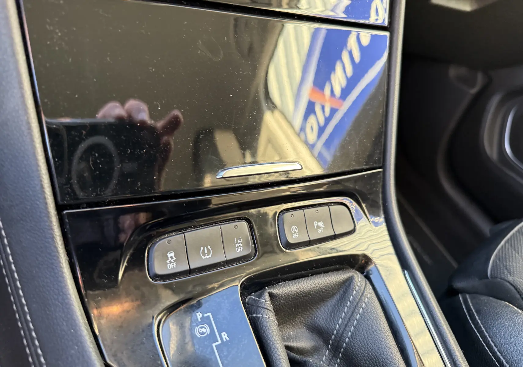 Gros plan sur la console centrale noire brillante de l’Opel Grandland X gris quartz, montrant les boutons de contrôle et le levier de boîte automatique.