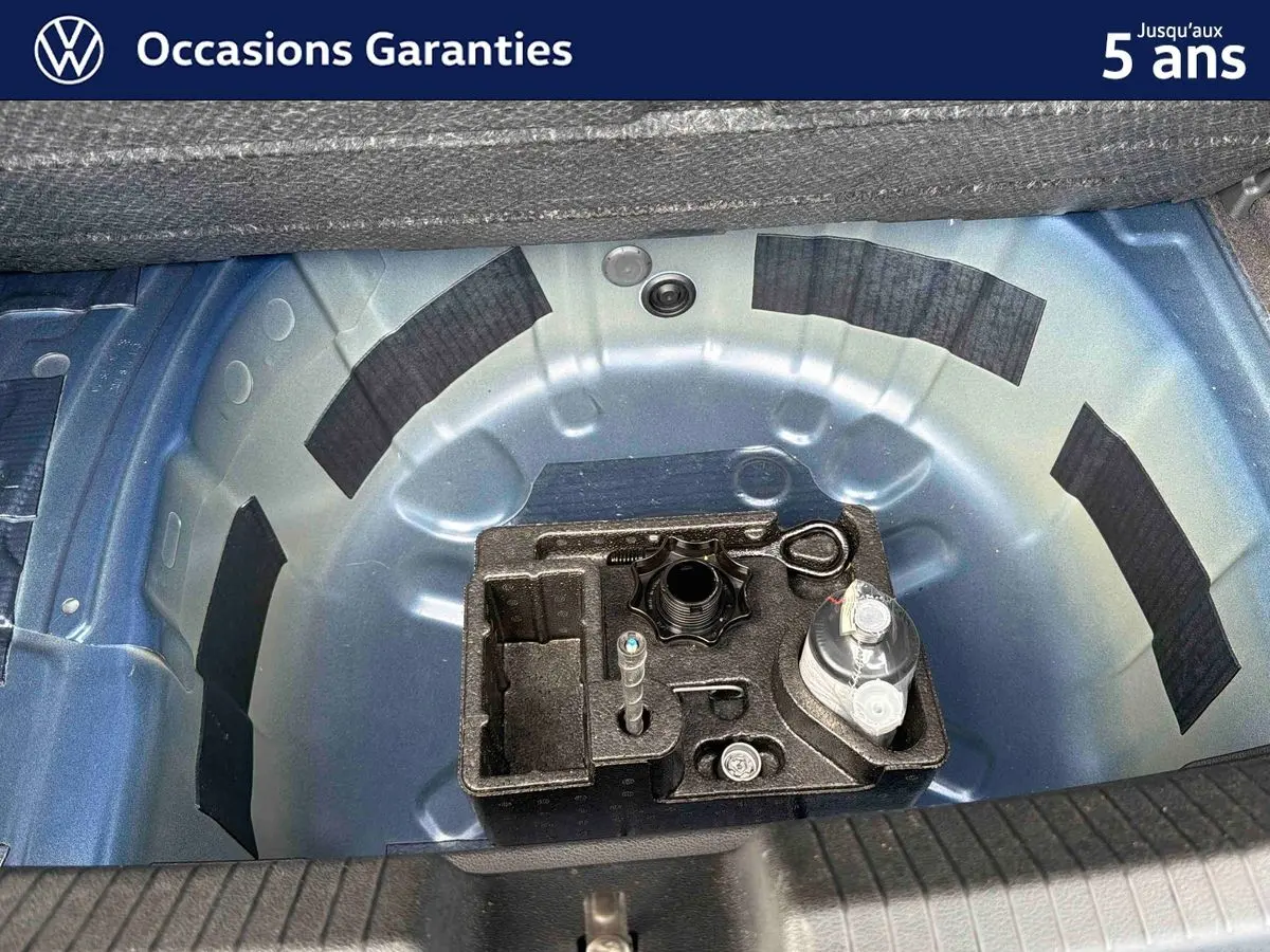 Vue plongeante sur le coffre ouvert d'une Volkswagen Polo bleue 2025, montrant la roue de secours et les outils.