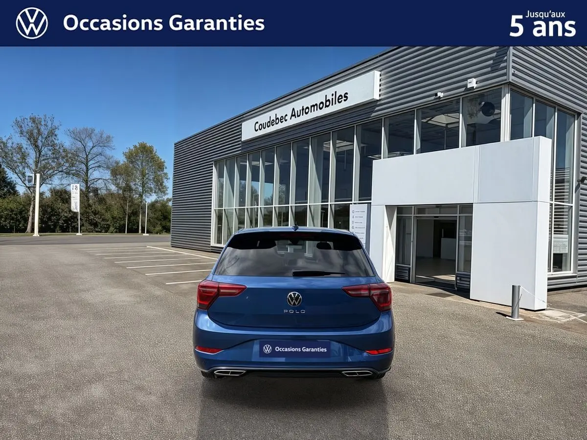 Vue arrière d'une Volkswagen Polo 2025 bleu récif métallisée, avec toit noir et vitres arrière surteintées, stationnée devant un showroom.